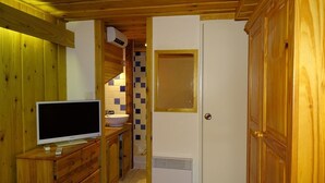 Une cuisine compacte avec des meubles en bois, un évier encastré, un téléviseur posé sur une commode en bois et un réfrigérateur blanc.