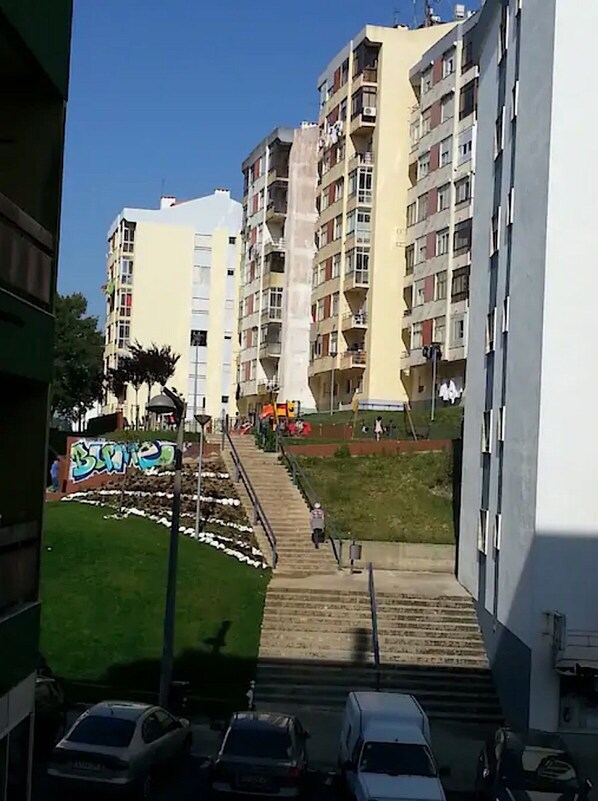 A multi-story residential building with balconies, a staircase leading to the entrance, and a small garden area with graffiti.