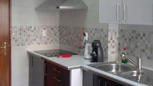 Une cuisine compacte équipée d’une cuisinière intégrée, d’un four à micro-ondes et d’un évier. Une porte en bois se trouve à gauche, et le mur derrière l’évier est recouvert de carreaux.