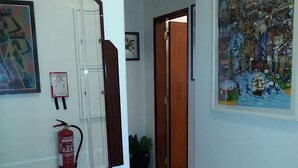 Un couloir avec une table en bois, un extincteur et un grand tableau représentant un paysage urbain accroché au mur.