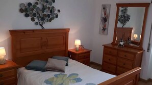 Une chambre à coucher avec un lit en bois, des tables de chevet, une commode, un miroir et des œuvres d’art murales.
