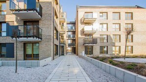 A modern apartment building with a central courtyard, featuring a tiled walkway and a small tree. - Modern Apartment | Parking, Balcony with View (Gdansk)