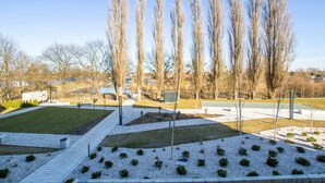 A landscaped area with pathways, trimmed bushes, and tall, leafless trees. - Modern Apartment | Parking, Balcony with View (Gdansk)