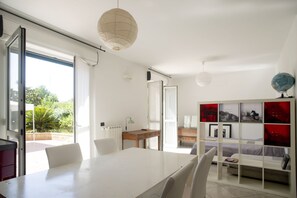 Quarto moderno e bem iluminado, com uma mesa de jantar, cadeiras, um radiador e uma estante com quadros emoldurados.