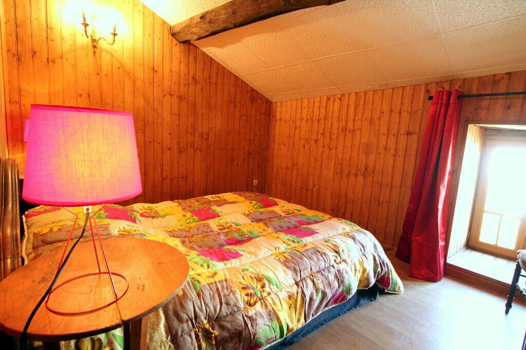 Ein Zimmer mit Holzpaneelen, einem Bett, einer Lampe und einem Fenster mit Vorhängen.