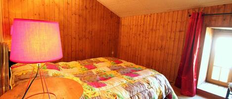 Ein Zimmer mit Holzpaneelen, einem Bett, einer Lampe und einem Fenster mit Vorhängen.