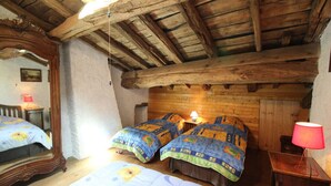 Ein rustikaler Raum mit freiliegenden Holzbalken, zwei Betten mit floralem Bettzeug, einem Spiegel und einer roten Lampe.
