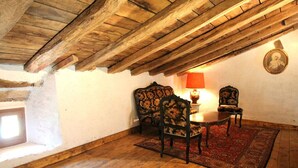 Ein rustikaler Raum mit Holzbalken an der Decke, einem runden Tisch mit Stühlen und einem roten Teppich mit Muster.