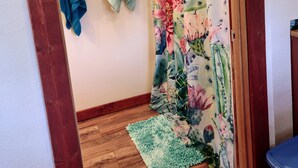 A bathroom with a shower curtain featuring a floral design, a wooden floor, and a green towel hanging on the wall. - Gnome away from home (Sweetwater)