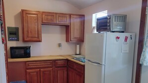 A compact kitchen with wooden cabinets, a microwave, a refrigerator, and a trash bin. - Gnome away from home (Sweetwater)