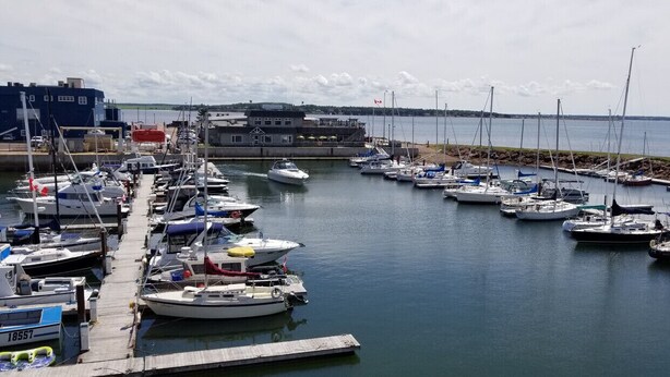A marina with various boats docked, a pier, and a building with a Canadian flag. - Downtown Summerside Jewel (Summerside, PE)