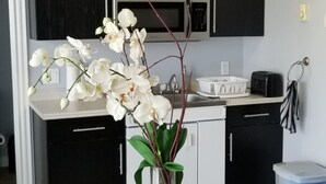 A kitchen with black cabinets, a microwave, and a sink. There is a vase with white flowers on a table with a red and white checkered tablecloth. - Downtown Summerside Jewel (Summerside, PE)