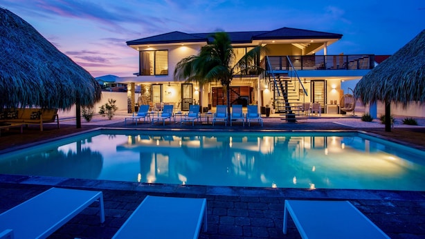 A modern two-story house with a swimming pool, lounge chairs, and thatched umbrellas. - Hasta La Vista Royal – Tropical 7BR Villa for Groups, Jan Thiel (Jan Thiel)