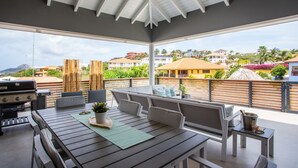 An outdoor patio with a dining table, chairs, a grill, and a view of the surrounding neighborhood. - Hasta La Vista Royal – Tropical 7BR Villa for Groups, Jan Thiel (Jan Thiel)
