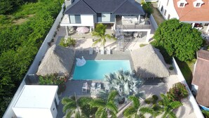 A modern house with a swimming pool, thatched umbrellas, and a well-maintained garden. - Hasta La Vista Royal – Tropical 7BR Villa for Groups, Jan Thiel (Jan Thiel)
