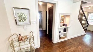 A hallway with a metal cart, a framed artwork, a door leading to another room, and a staircase.