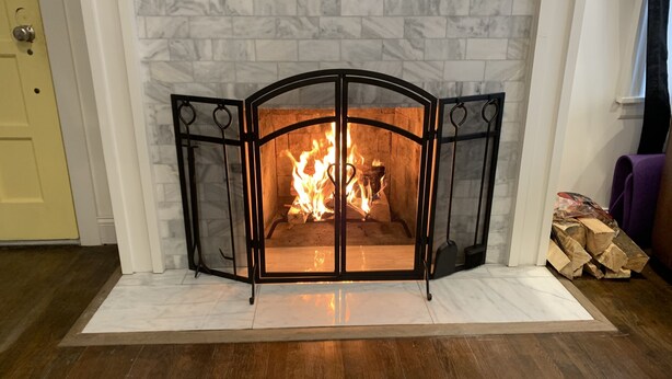 A fireplace with a white marble surround, a black metal screen, and a fire burning inside.