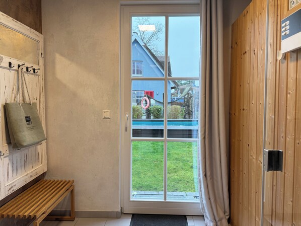 A room with a bench, a door with a view of a blue house, and a wooden wall.