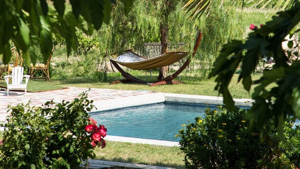 A pool area with a hammock, chairs, and lush greenery.