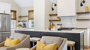 Une cuisine moderne dotée d’un îlot central, de deux tabourets de bar et d’un réfrigérateur.