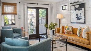 Un salon comprenant un canapé, des fauteuils, une table basse en verre et une grande fenêtre avec des stores.