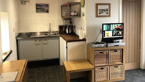 A compact kitchen with a sink, stove, and microwave. There's a small dining table and a television on a wooden stand.
