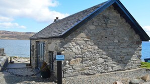 A stone cottage with a sloped roof, a small porch, and a sign indicating it is a holiday lake accommodation.