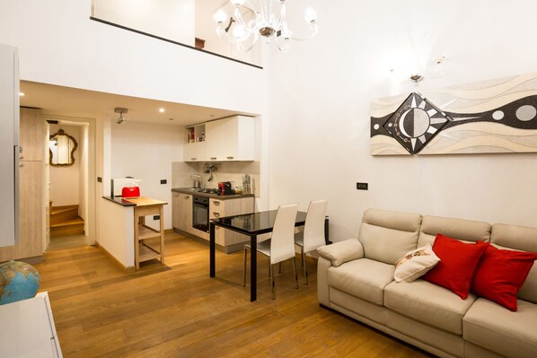 A modern living room with a beige sofa, a dining table with chairs, and a kitchen in the background. - Triangolo D'Oro Apartment (Genova)