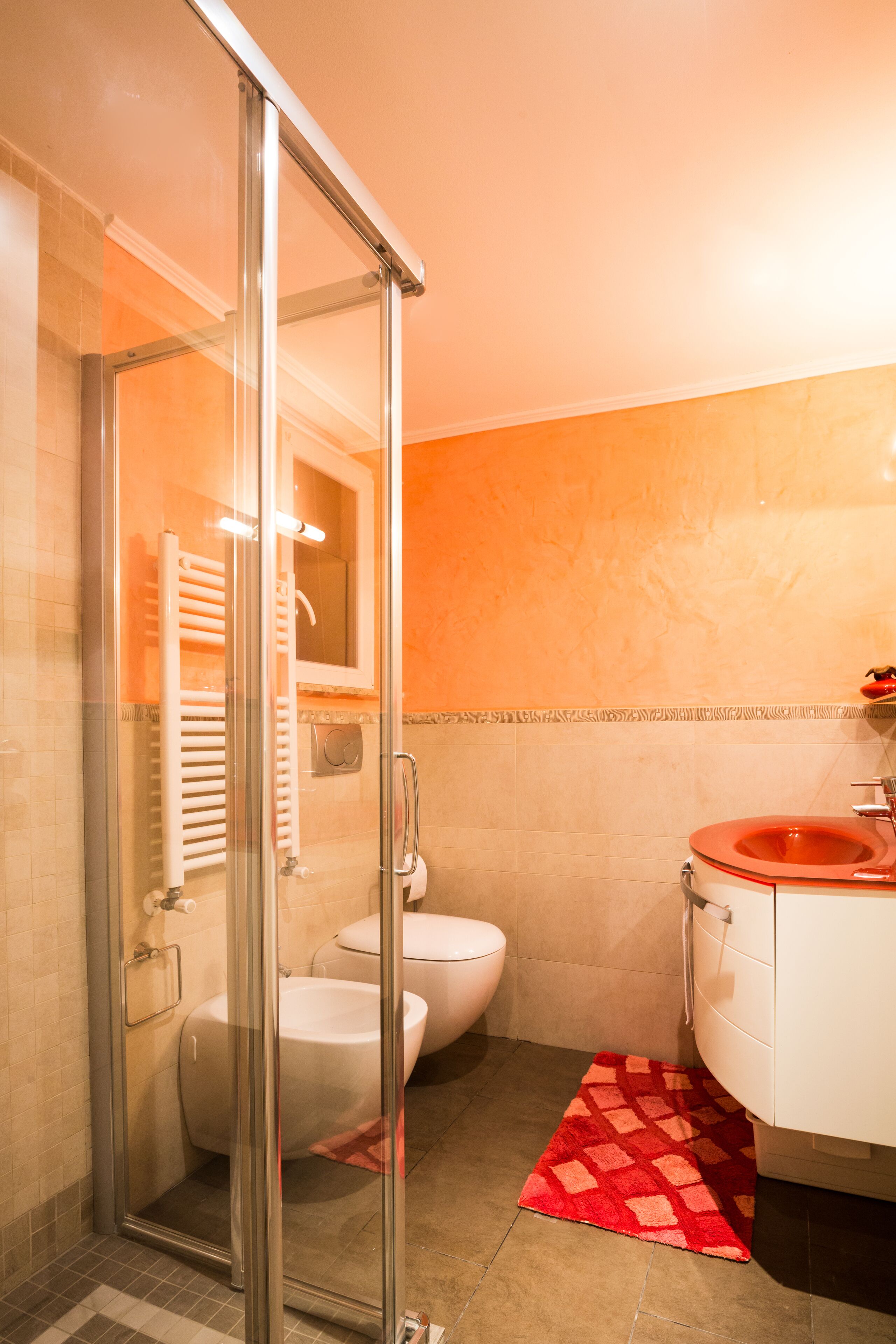 Une salle de bain avec une douche à parois de verre, des toilettes blanches et un lavabo rouge.