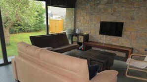 A modern living room with a beige sofa, a coffee table, and a flat-screen TV mounted on a stone wall.