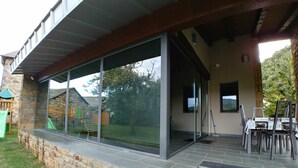 A modern building with a stone exterior, large glass windows, and a covered outdoor area with a table and chairs.