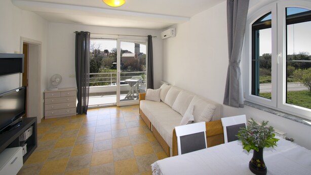 A modern living room with a sofa, a TV, a fan, and a dining table with a vase of flowers. - Comfortable and charming apartment, beside the nature park (Premantura)