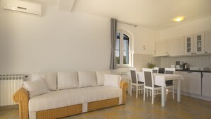 A modern kitchen with white cabinets, a dining table with chairs, a white sofa, and a window with curtains. - Comfortable and charming apartment, beside the nature park (Premantura)