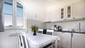 A kitchen with white cabinets, a dining table with chairs, a window, and a radiator. - Comfortable and charming apartment, beside the nature park (Premantura)