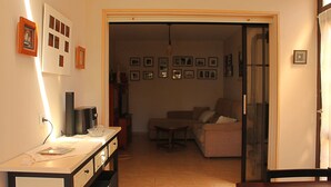 Una sala de estar con sofá, una mesa de centro y televisor. Hay cuadros en la pared y una puerta que da a otra habitación.