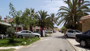 Una calle residencial con coches aparcados, palmeras y casas.