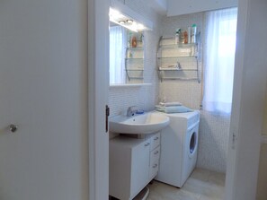 Ein kleines, weißes Badezimmer mit Waschbecken, Spiegel und Waschmaschine.