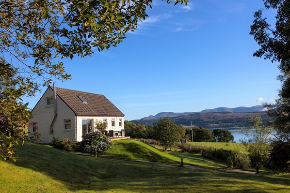 Una casa con tetto spiovente, un portico e vista su un lago e montagne sullo sfondo.