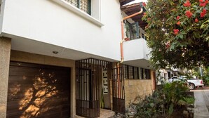 A residential building with a closed garage door, a gated entrance, and a small garden area with plants and a tree with red flowers. - Alameda House   a beautiful apartment located in Medellín (Medellín)