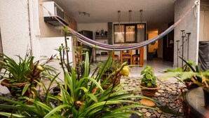 A hammock in a garden area with potted plants and a dining area in the background. - Alameda House   a beautiful apartment located in Medellín (Medellín)