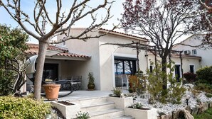 Une maison moderne dotée d’un patio, d’un espace salon extérieur et d’un jardin avec des marches menant à l’entrée.