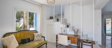 Una sala moderna con un sofá, un escritorio y una silla. Se ve una escalera con barandilla y vistas al exterior.