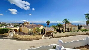 Una zona residenziale costiera con edifici in stile mediterraneo, cielo azzurro limpido e vista sul mare.