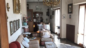 A spacious living room with a red sofa, a chandelier, and a dining area with a cabinet and table. - Penthouse Anna, in the center of a small town with a splendid sea view (Ortona)