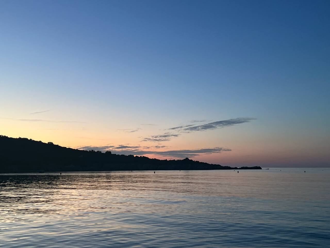 Rustig water met een vage silhouet van de kustlijn tijdens zonsondergang.