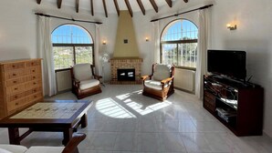 Un salon spacieux avec une cheminée, deux fauteuils, un téléviseur et un meuble en bois.