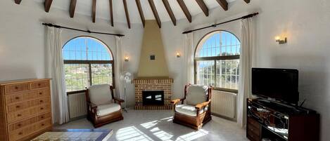 A spacious living room with a fireplace, two armchairs, a TV, and a wooden cabinet.