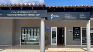 Un immeuble commercial doté d’un toit en tuiles, d’une entrée en verre et d’une enseigne publicitaire annonçant des services de vente, de location et de construction.