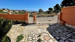Une entrée fermée par un portail, avec un chemin pavé de pierres menant à un quartier résidentiel où se trouvent des maisons et des arbres.