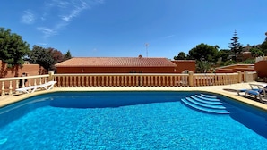 Une piscine d’un bleu éclatant, bordée d’une terrasse carrelée et entourée d’une clôture en bois, avec des chaises longues à proximité.